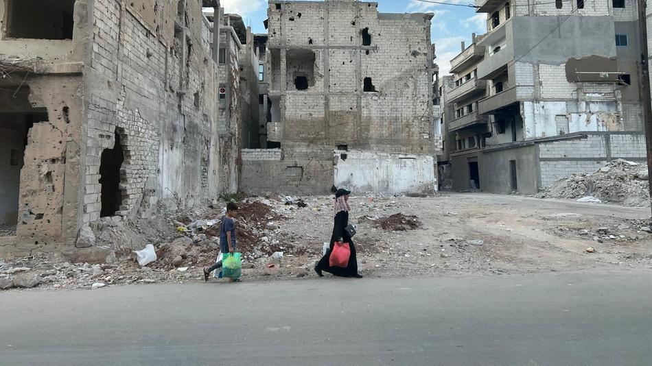 Eine Frau und ihr Kind laufen vor zertrümmerten Häusern in Homs
