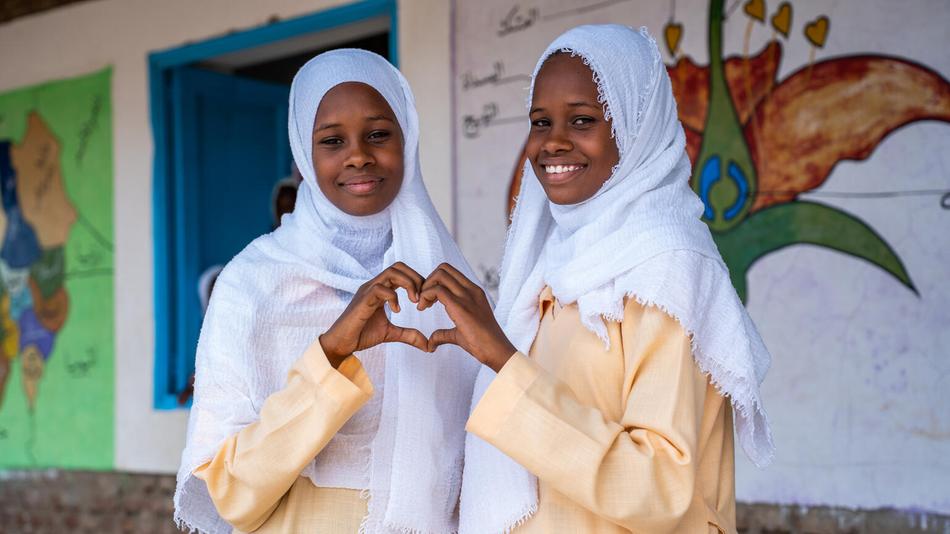 Foto von zwei Schülerinnen vor einer von UNICEF erbauten Schule im Sudan